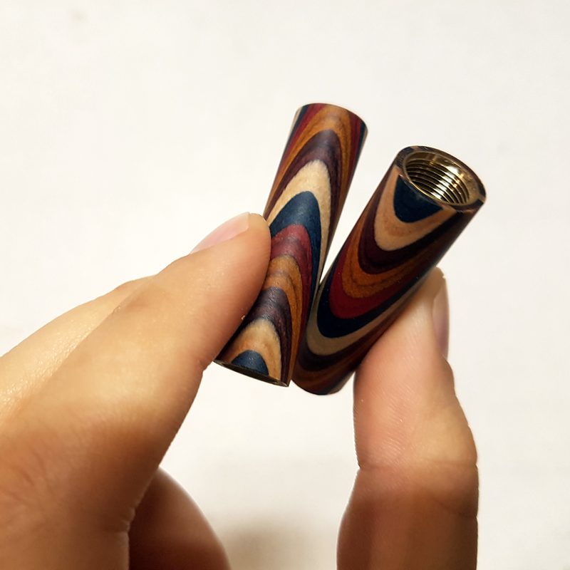 Due fusti in laminato multicolore appena torniti, tenuti tra le dita, con i tubi in ottone all'interno