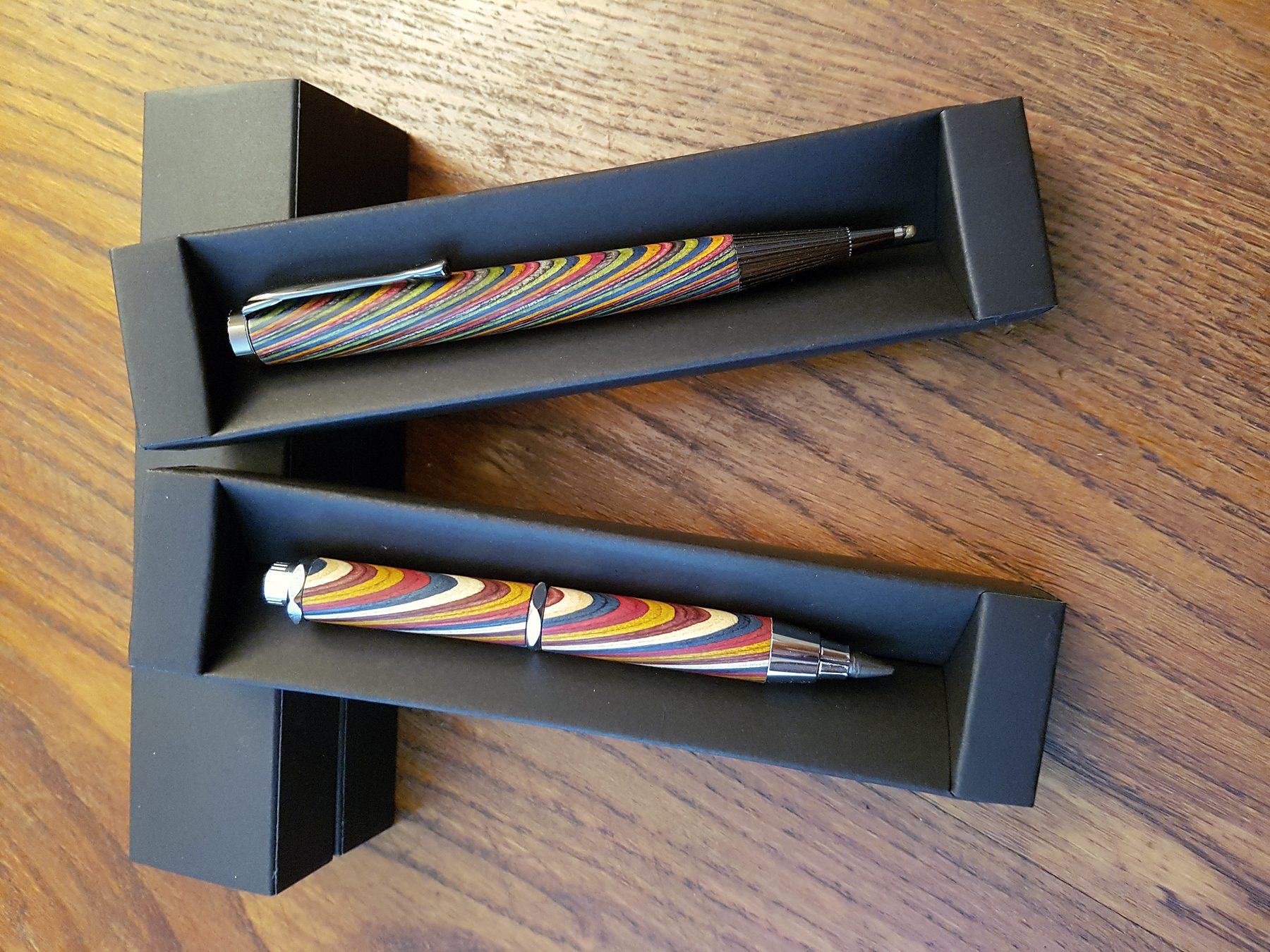 Una penna a sfera e una matita a mina larga in laminato multicolore, nelle loro scatole nere su un tavolo di legno